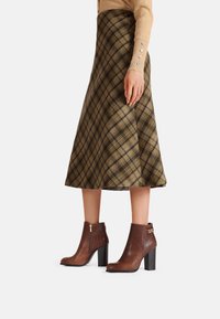 Stivali ankle in pelle marrone con finitura testurizzata, cerniera laterale e tacco a blocco, abbinati a una gonna a quadri in tonalità verdi e marroni.