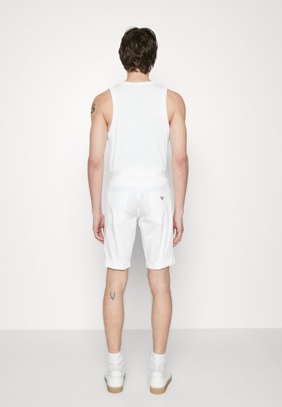 Hvit ermeløs skjorte og hvite shorts med rullet kant, med en logo på baklommen, vist fra baksiden.