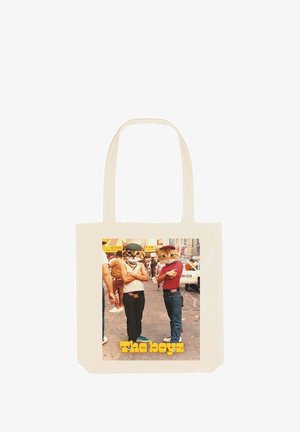 Kriešana Tote soma krēmkrāsā ar taisnstūra grafiku, kurā redzami divi karikatūru kaķi un teksts "The boyz", fona attēlā redzama krāsaina ielas aina.