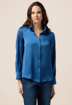 Camicetta blu in satin con colletto, maniche lunghe e orlo dritto. Presenta una texture lucida e dettagli con bottoni argentati.