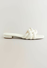 Sandales plates blanches avec une tige en tissu tressé, design ouvert à l'avant, et un talon bas. Finition texturée et style minimaliste.
