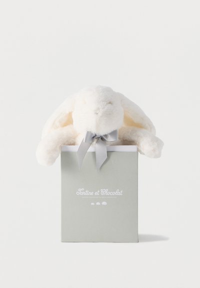 Μαλακό λευκό λούτρινο κουνελάκι με πεσμένα αυτιά και γκρι φιόγκο, καθισμένο μέσα σε γκρι κουτί με την ετικέτα «Tartine et Chocolat» πάνω σε λευκό φόντο.