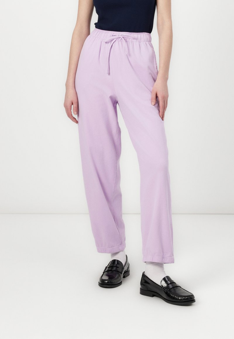 Lilac jogger pants with an elastic waistband and adjustable drawstring, featuring a loose fit and cuffed ankles, paired with black loafers.