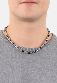 Collana di metallo con catena che presenta anelli neri e argento alternati, indossata attorno al collo sopra un maglione grigio.