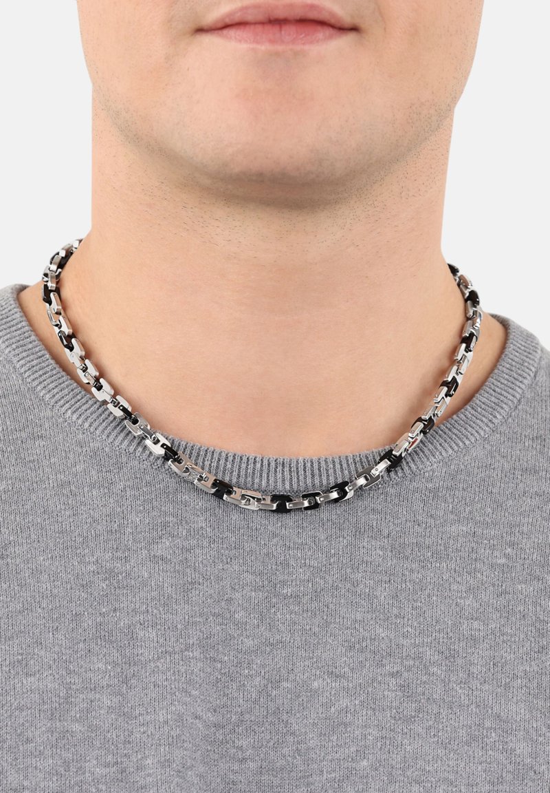 Metallkettenschnurr mit abwechselnd schwarzen und silbernen Gliedern, um den Hals über einem grauen Pullover getragen.