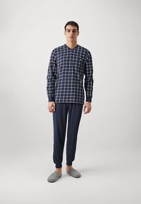 Top de manga larga azul marino con patrón de cuadrícula blanca, diseño de cuello en V; combinado con pantalones azul marino; modelo lleva zapatillas grises.