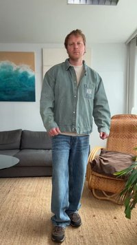 Vihreä farkkutakki vaaleanbeige paidan päällä, yhdistettynä löysiin sinisiin farkkuihin ja ruskeisiin lenkkareihin. Yksinkertainen muotoilu, takissa näkyvät taskuyksityiskohdat.