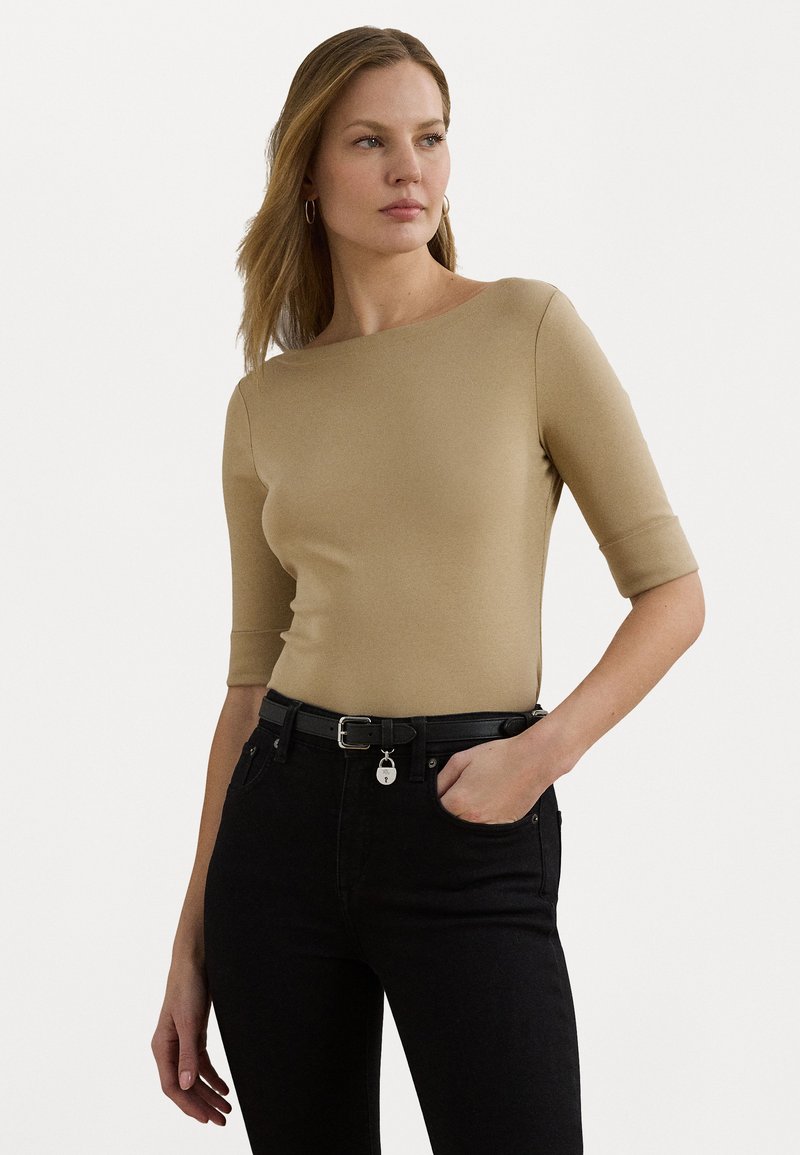 Beige tettskjorte med tre kvart ermer, rund hals, jevn tekstur. Kombinert med høy midje svarte jeans og et svart belte.