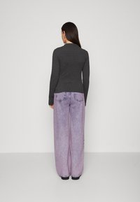 Mørkegrå ribbestrikket langermet topp kombinert med lyse lilla vide jeans. Antrekket har et enkelt design med minimale detaljer.