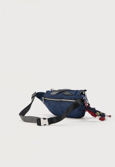 Σακίδιο μέσης σε ναυτικό μπλε με ασημί φερμουάρ, μαύρο ρυθμιζόμενο λουρί και προσαρτημένη πολύχρωμη μπρελόκ σχοινί σε ανοιχτό φόντο.