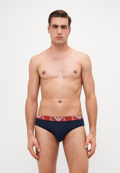 Boxers pour hommes bleu marine avec une ceinture rouge contrastante arborant une marque blanche. Tissu doux et lisse avec une coupe ajustée. Design de boxer classique.