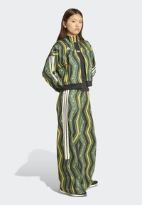 Survêtement à motifs en vert, jaune et noir avec un design en zigzag. Comprend une veste à fermeture éclair et un pantalon large avec des bandes blanches sur les côtés.