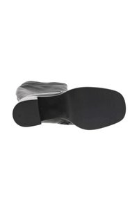 Botte en cuir noir avec un bout rond, un empeigne flexible et une semelle plate en caoutchouc ; le dessous présente une texture nervurée pour une meilleure adhérence.