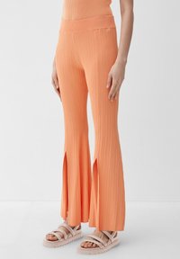Geribbelde flarebroeken in lichtoranje. Heeft een hoge taille en zijslits aan de zoom. Gecombineerd met sandalen in neutrale tinten.