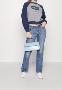 Sudadera recortada gris y azul marino con logo, bolso de imitación de cocodrilo azul claro, jeans acampanados de lavado claro, zapatillas blancas con suelas texturizadas.