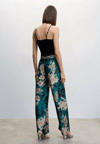 Camisole noire à fines bretelles associée à un pantalon large à jambes larges couleur sarcelle avec de grandes fleurs crème et noires, texture satinée lisse et taille ceinturée.