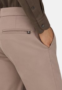 Ružovo-hnedé nohavice majú elegantný dizajn so zadošným vreckom a malou značkovou nálepkou. Tkanina má jemnú textúrovanú úpravu.