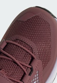 Zapatilla deportiva color burdeos con parte superior de malla texturizada, acentos sintéticos y un cuello acolchado. Incluye cordones negros y una suela blanca.