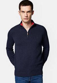 Granatowy sweter dzianinowy z szyją na zamek, z czerwoną wewnętrzną kołnierzem. Klasyczny fason z prążkowanymi mankietami i dołem.