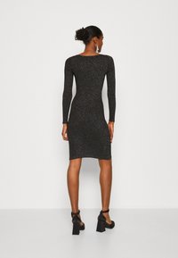 Black long-sleeve dress with a fitted silhouette, made of sparkly textured material, knee-length, worn with black block-heeled shoes.