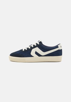 Blue denim low-top sneaker with a white leather accent and cream rubber sole; features round laces and textured detailing on the sole.