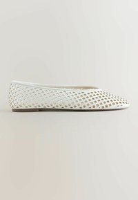 Chaussure plate blanche avec bout pointu et motif de découpes en forme de diamants sur toute la partie supérieure.