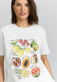 Witte katoenen t-shirt met kleurrijke fruitillustraties: citroenen, frambozen, avocado's, granaatappels, papaja's, ananassen en watermeloenen.