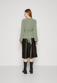 Green, textured blouse with long sleeves and back tie detail, paired with a black leather midi skirt and knee-high black boots.