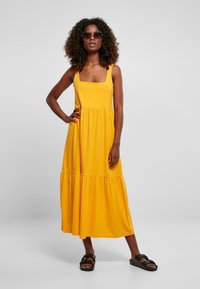 Geel mouwloos maxi-jurk met een vierkante halslijn en een gelaagde rok. Gemaakt van zachte stof, met een losse pasvorm en een casual stijl.