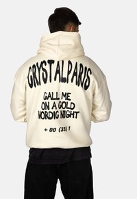 Felpa oversize crema con grande testo nero sul retro: "CRYSTALPARIS," "CHIAMAMI IN UNA NOTTE NORDICA D'ORO," e "+00 (33) 1."