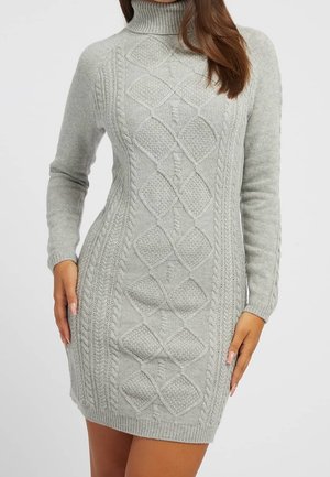 Mujer con un vestido suéter de cuello alto tejido en color gris claro, con motivos de trenzas y rombos, mangas largas, y puños y dobladillo acanalados.