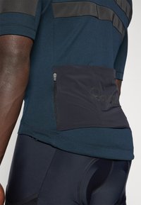 Maillot de cyclisme bleu marine avec des manches courtes, des accents noirs texturés et une poche zippée à la taille pour le rangement.
