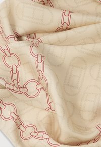 Krémový šátek s červeným vzorem řetězových článků. Má hladkou texturu a splývavou látku, s potiskem odkazů různých velikostí a tvarů.