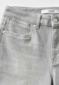 Light gray denim jeans with a smooth texture, featuring a front pocket, silver hardware, and a stitched waistband label.