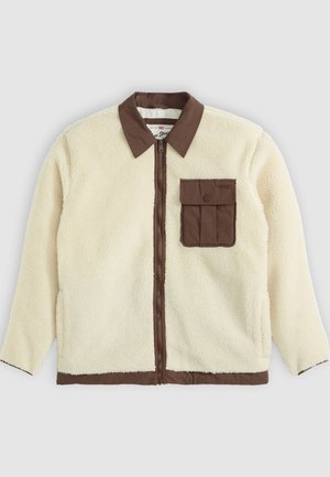 White fleece jacket with a brown collar, front zipper, and a chest pocket featuring a flap. The texture is soft with a shaggy appearance.