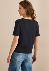 Haut texturé bleu marine à manches courtes, décolleté carré et motif horizontal. Associé à un jean en denim bleu clair.