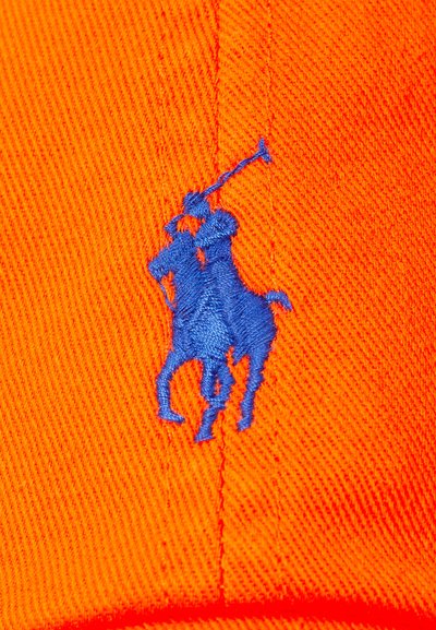 Oranžinė kepurė su iškilniu mėlynu išsiuvinėjimu, vaizduojančiu polo žaidėją. Audinys turi tekstūrą su matomais siuvimo detalėmis.