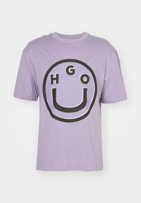 Lilla bomulds-T-shirt med et stort cirkulært sort grafisk motiver med bogstaverne "HGO" og en U-form, korte ærmer og en rund hals.