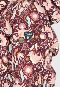 Bordeaux stoffen met een bloem- en dierenpatroon in roze, blauw en geel. Inclusief een zwart Zigzag-logo patch.