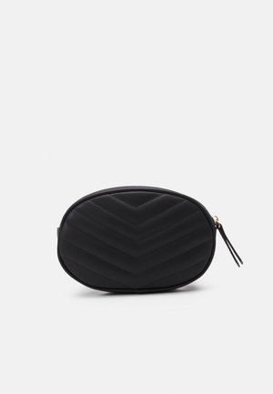Sac ovale noir matelassé avec motif chevron et fermoir à glissière avec une languette noire assortie sur fond blanc.