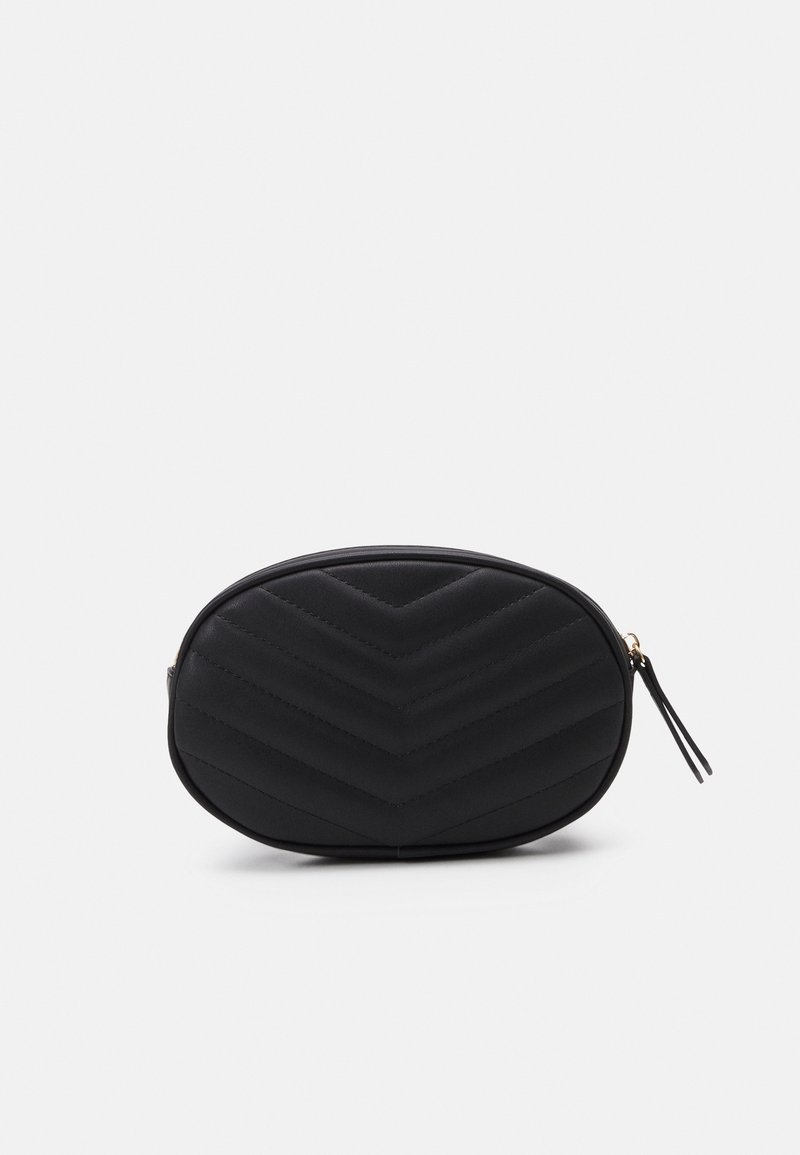 Sac ovale noir matelassé avec motif chevron et fermoir à glissière avec une languette noire assortie sur fond blanc.