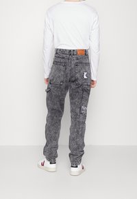 Pantalones cargo de mezclilla en negro desgastado con un ajuste relajado, con múltiples bolsillos, parche con logo y detalles de costuras en contraste.