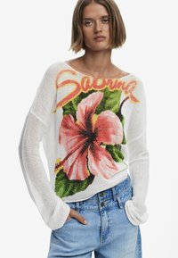 Pull bianco a maglia con una grande grafica floreale rosa e foglie verdi, con la scritta "Sabrina" sopra. Maniche lunghe e larghe, tessuto leggero.