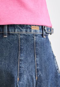 Jeans din denim de culoare albastru închis, cu croială dreaptă, având o etichetă din piele bej pe care este gravat "HUGO" și detalii de cusătură minimaliste.