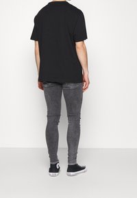Camiseta de algodón negra combinada con jeans ajustados grises. La camiseta tiene mangas cortas y los jeans presentan una textura desgastada y bolsillos traseros.