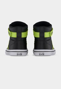 Μαύρα και νέον πράσινα ψηλά αθλητικά παπούτσια Converse All Star, εμφανιζόμενα από πίσω σε λευκό φόντο.