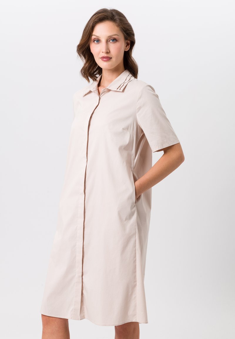Robe beige clair en coton avec un devant à boutons, des manches courtes et des poches latérales. Elle présente un col classique et une coupe décontractée.