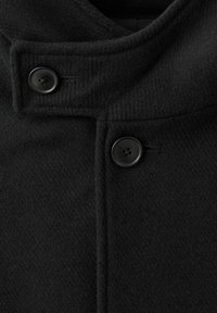 Abrigo de lana negra con cuello alto, dos botones negros en la parte delantera y una tela de textura suave. Diseño limpio con detalles mínimos.