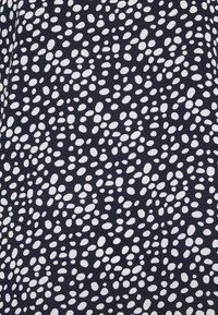 Námořnická látka s texturovaným vzorem nepravidelných bílých teček. Materiál se zdá být hladký s mírným leskem.