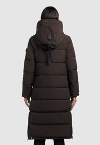 Long manteau en duvet brun avec une capuche, présentant des sections matelassées, des côtés zippés et une étiquette de marque proéminente à l'arrière.